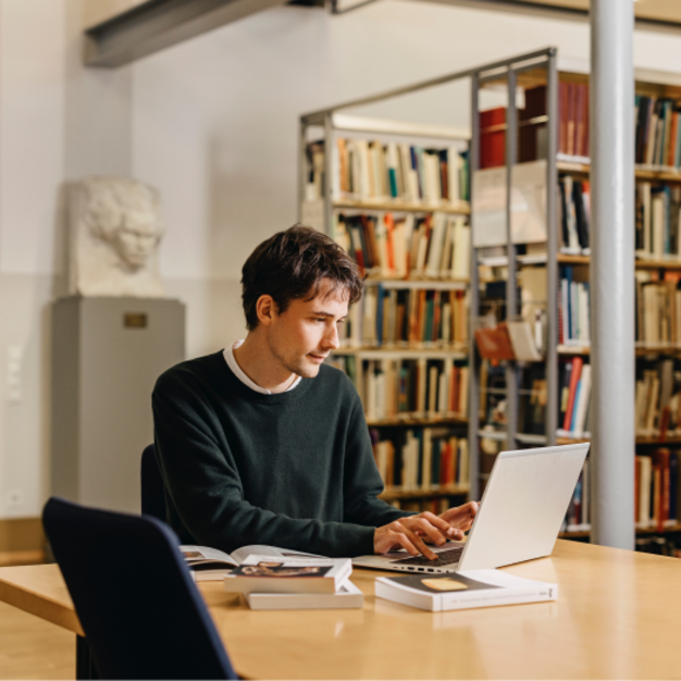 Person arbeitet mit Laptop an einem Tisch in einer Bibliothek
